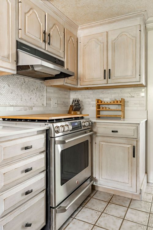 Kitchen range wall with marble herringbone backsplash and cream raised-panel cabinets
