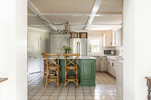 View into a beamed-ceiling kitchen with chandelier, stainless fridge and green island