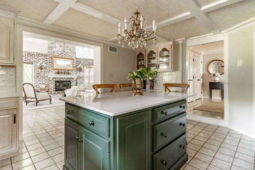 Kitchen island opens to a living room with exposed brick fireplace and chandelier