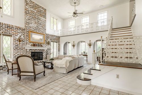 Two-story living room with an exposed brick fireplace wall and wrought iron balcony railing