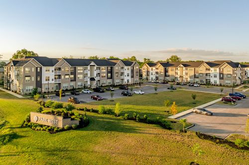 Aerial view of the apartment complex with entry sign, parking and lawn at dusk
