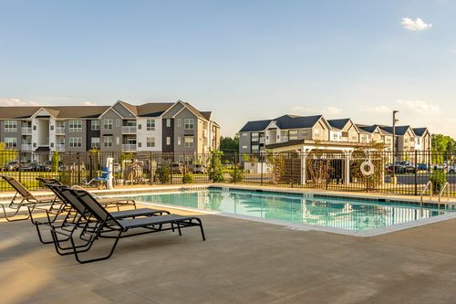 Pool deck with lounge chairs, a pergola and apartment buildings in the background