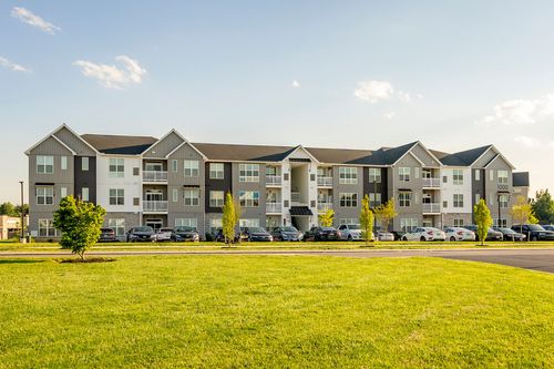 Wide exterior view of a three-story apartment building beyond an open lawn