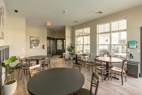 Community lounge with round tables and tall windows near the entry