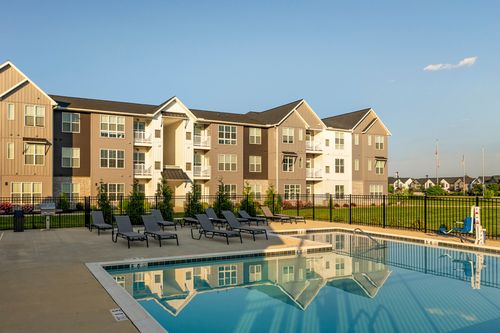 Wide view of an outdoor pool with lounge chairs and apartment buildings behind