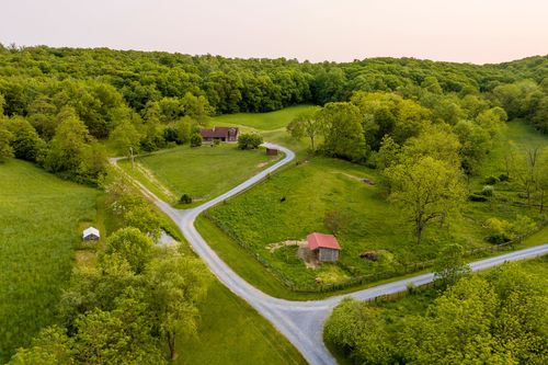 Aerial view of a farmhouse and red-roofed barn along a winding driveway through green hills