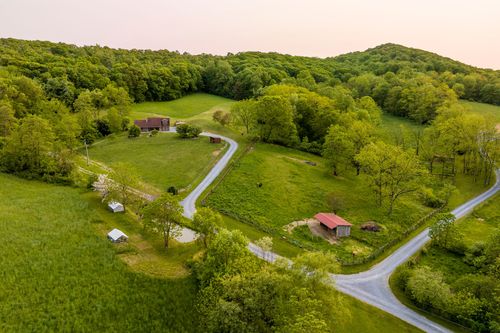 Aerial view of a farmhouse set among rolling green pasture and wooded hills