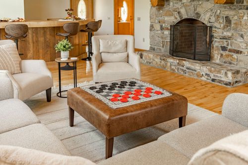 Living room with a leather ottoman, armchairs and a stone fireplace mantel