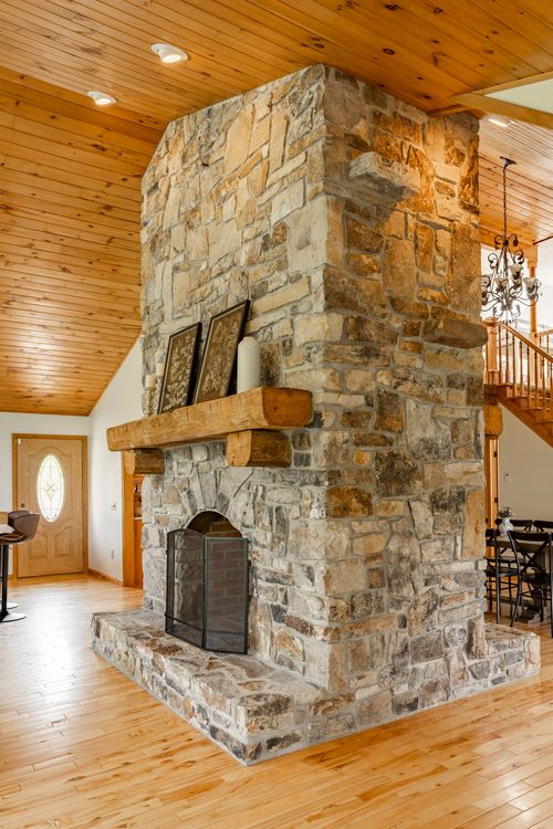Detailed view of a stone fireplace with a wood mantel and chandelier beyond