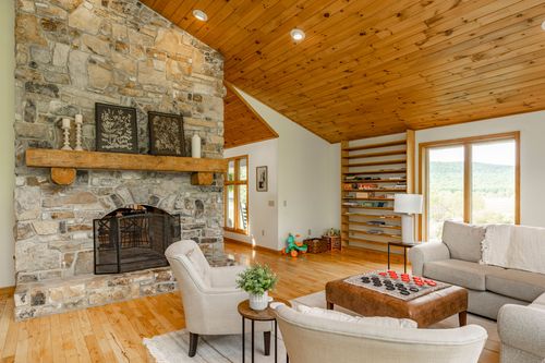 Living room with a stone fireplace, board-game shelving and mountain views through large windows