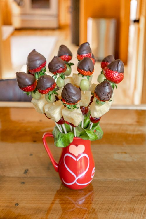 Close-up of chocolate-covered strawberry and pineapple skewers in a red pitcher