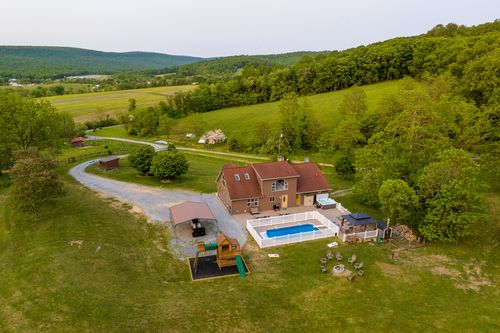 Aerial view of a farmhouse with a pool and play area overlooking a scenic valley at sunrise