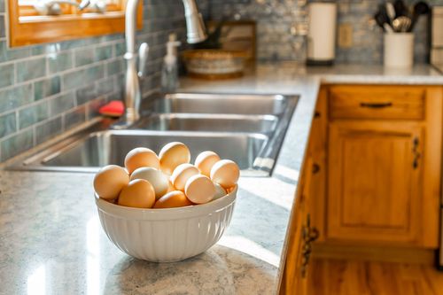 Bowl of farm-fresh eggs beside a stainless steel sink and tile backsplash