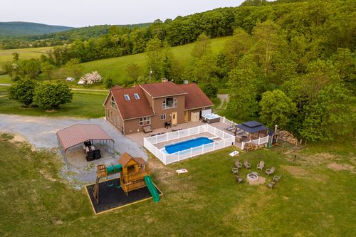 Aerial view of a farmhouse with a fenced pool, carport and children's play structure