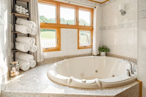 Round jetted tub with granite surround, folded towels on a ladder rack and a garden view window