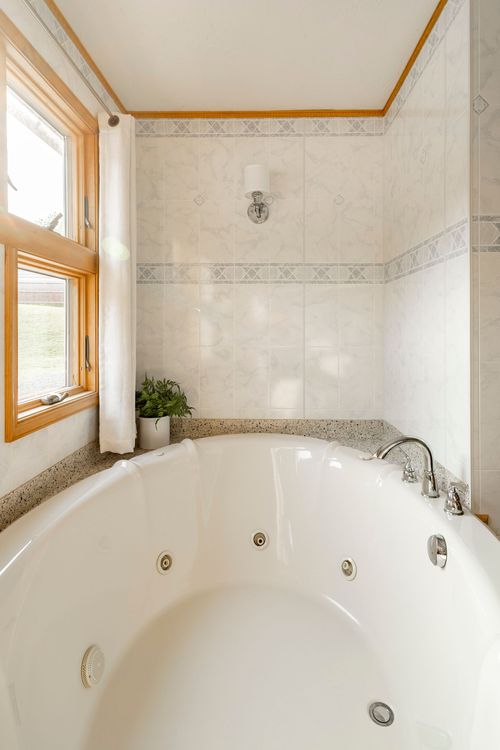 Jetted tub in a marble-tiled alcove with a wall sconce and potted plant on the ledge