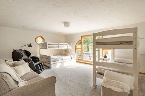 Loft bedroom with a built-in bunk bed, gray recliner and arched window overlooking the lawn