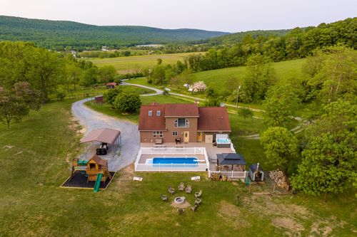 Aerial view of a farmhouse with a pool and fire pit seating overlooking rolling hills