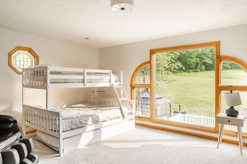 White bunk bed beside a round-top window with a sweeping green lawn view