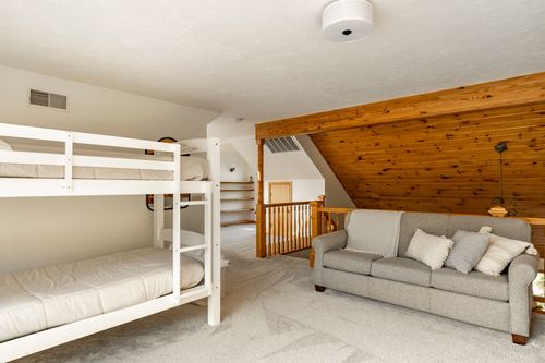 Bunk room with a gray sofa and knotty pine accent wall under a vaulted ceiling