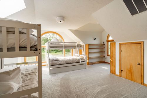 Bunk beds beneath a dormer window with built-in shelving and a stained wood door