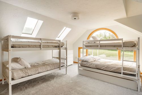 Twin bunk beds under skylights with an arched window framing the yard