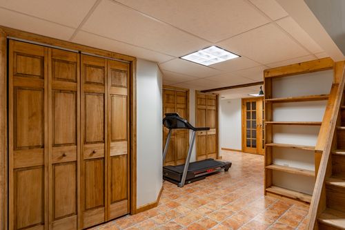 Finished basement hallway with built-in wood closets, open shelving and a home gym beyond