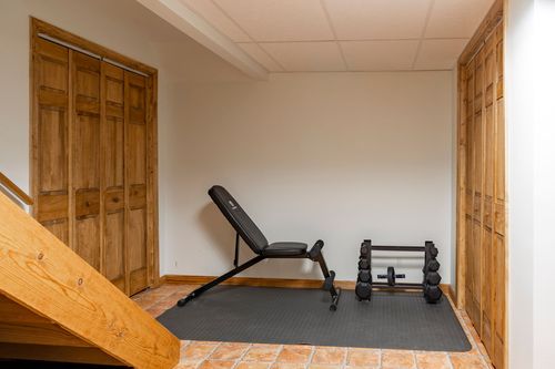 Basement home gym with an adjustable weight bench and dumbbell rack on tile flooring