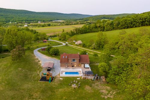 Aerial view of a farmhouse with a pool and playground framed by open farmland