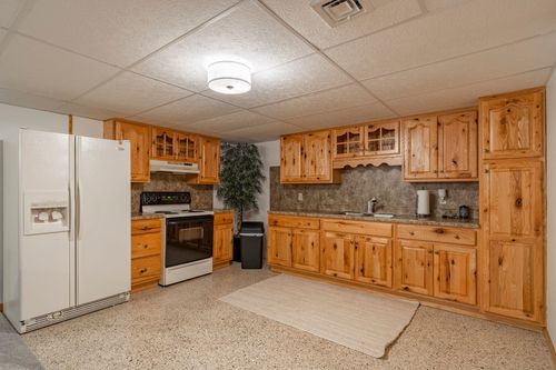 Basement kitchen with oak cabinetry, tile backsplash and a white refrigerator