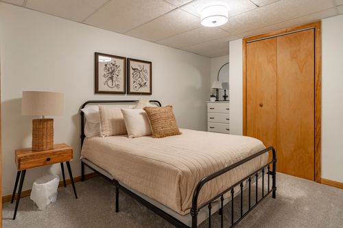 Bedroom with a black metal bed frame, botanical prints and a wood-paneled closet