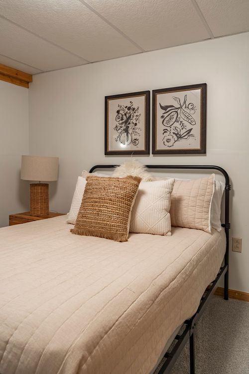 Twin bed with cream linens, a woven accent pillow and framed botanical artwork above