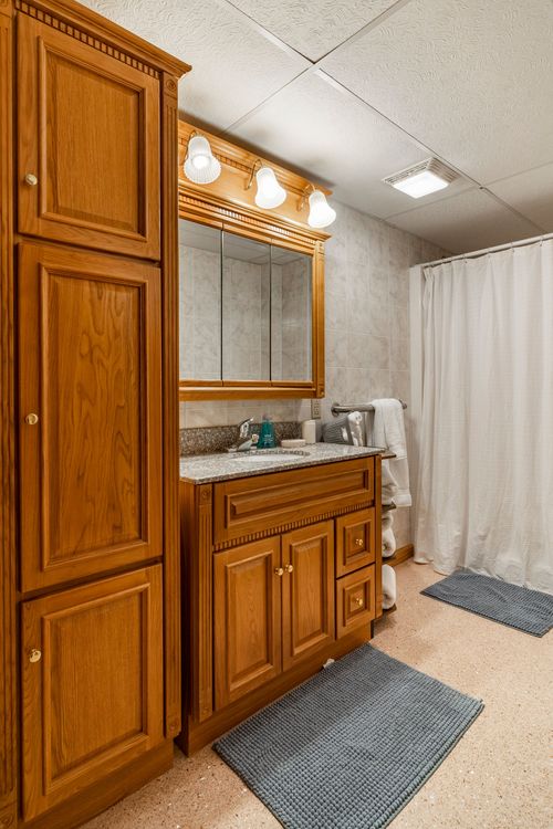 Bathroom with a wood vanity, lighted mirror and a shower behind a white curtain