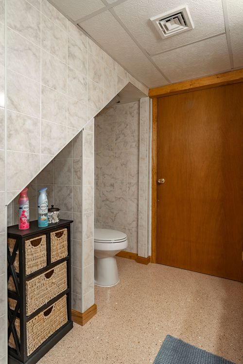 Under-stair powder room with a toilet, wicker storage baskets and a wood door