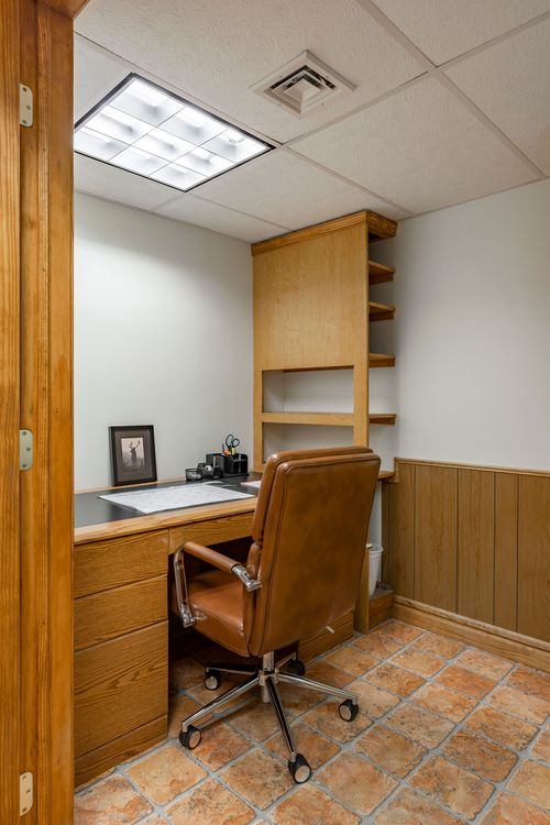 Home office with a built-in wood desk, open shelving and a leather task chair