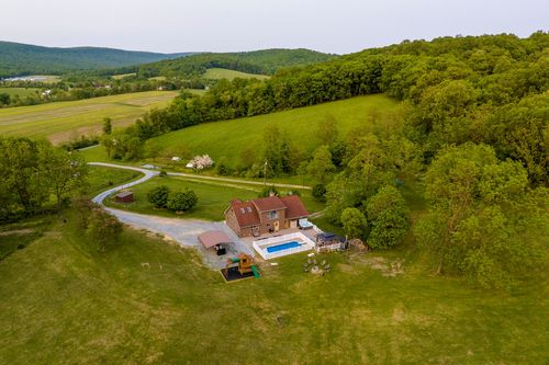 Aerial view of a farmhouse with a fenced pool patio overlooking distant farmland