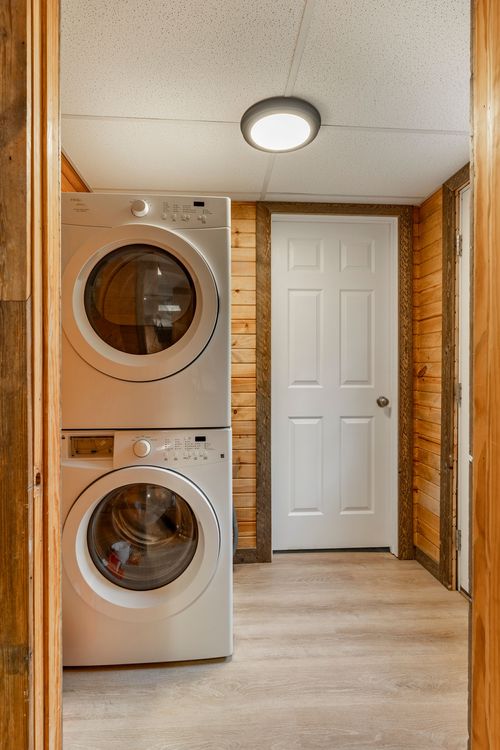 Laundry nook with a stacked white washer and dryer beside a wood-paneled hallway
