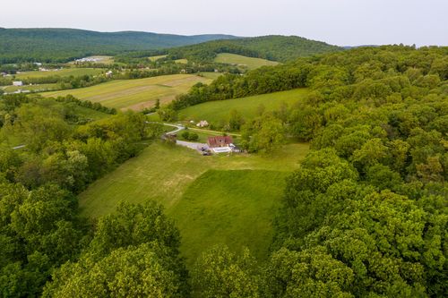 Aerial view of a farmhouse tucked into a wooded hillside clearing