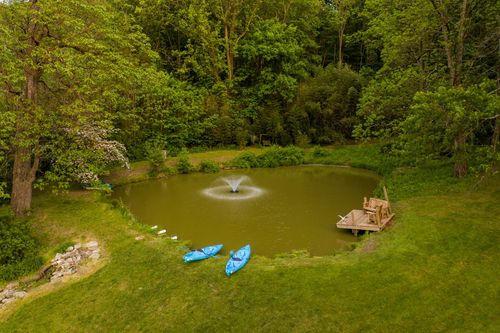 Aerial view of a wooded pond with a fountain, dock and kayaks along the shore