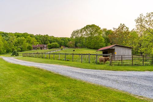 Aerial view of a winding gravel driveway through green farmland with a small barn