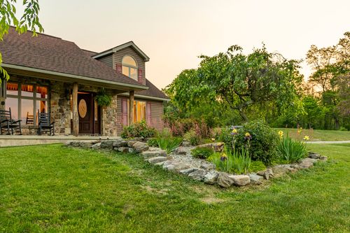 Exterior of a two-story farmhouse with a stone-accented covered porch and pink shutters