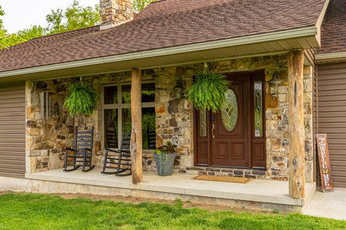 Stone farmhouse entry with a covered porch, rocking chairs and a landscaped garden bed