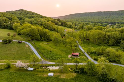 Aerial view of a farmhouse along a winding gravel driveway framed by green hills