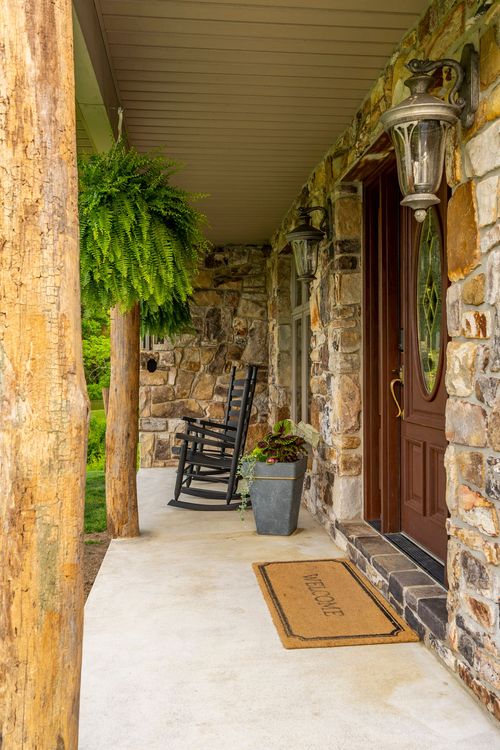 Covered log-post porch with rocking chairs, hanging ferns and a stone-accented entry