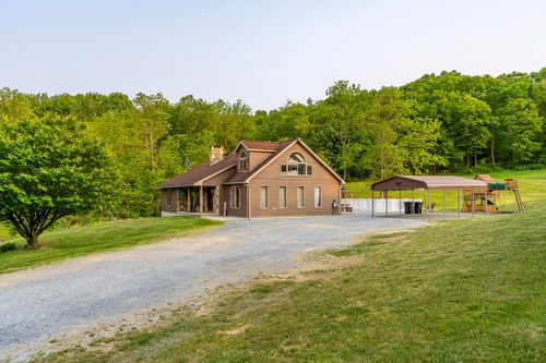 Exterior of a brown farmhouse with an arched dormer window beside a gravel driveway