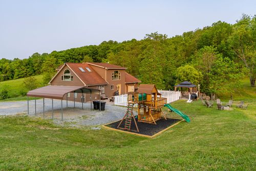 Aerial view of a farmhouse with a carport and children's play structure at dusk