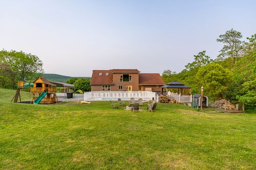 Aerial view of a farmhouse backyard with a white picket fence, fire pit and play area
