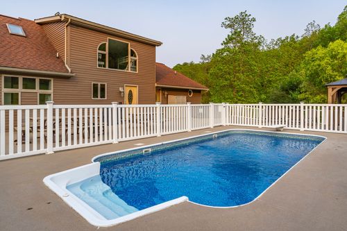 In-ground swimming pool with white picket fencing beside a two-story brown home