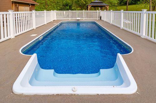 In-ground swimming pool with white vinyl fencing and steps into the shallow end