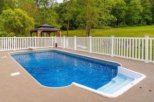 In-ground swimming pool with a white picket fence and wooden gazebo beyond